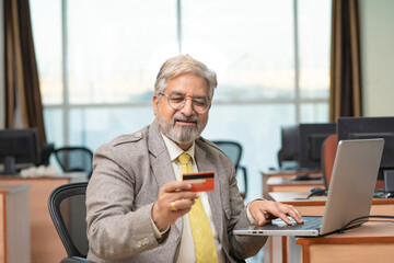 Senior Businessman using laptop and bank card at office