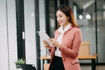 Obraz premium Confident Asian woman with a smile standing holding notepad and tablet at the office..