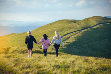 Fototapeta na wymiar Three Young Girl Friends Walk Together Holding Hands into Beautiful Mountain Landscapes