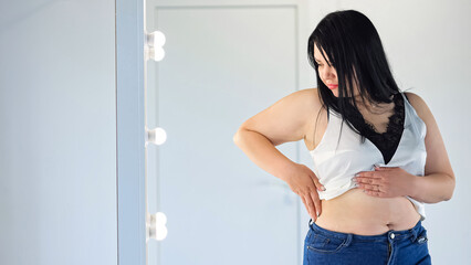 Chubby woman in t-shirt feeling insecure in own body touches fat folds on belly. Black-haired...