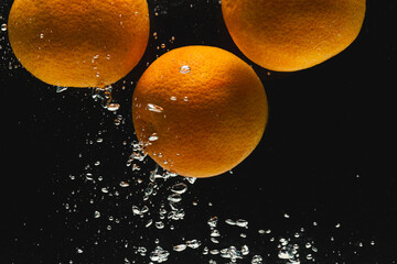 Close up of oranges falling into water with copy space on black background