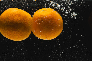 Close up of oranges falling into water with copy space on black background