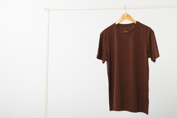 Fototapeta premium Brown t shirt on hanger hanging from clothes rail with copy space on white background