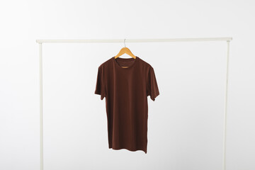 Fototapeta premium Brown t shirt on hanger hanging from clothes rail with copy space on white background