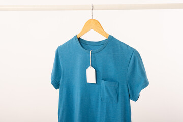 Obraz premium Blue t shirt with tag on hanger hanging from clothes rail with copy space on white background