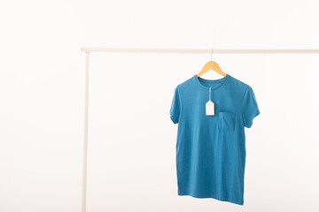 Naklejka premium Blue t shirt with tag on hanger hanging from clothes rail with copy space on white background