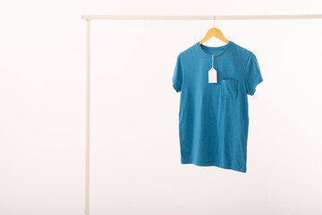 Fototapeta premium Blue t shirt with tag on hanger hanging from clothes rail with copy space on white background