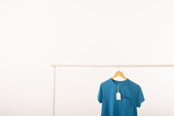 Obraz premium Blue t shirt with tag on hanger hanging from clothes rail with copy space on white background