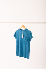 Fototapeta premium Blue t shirt with tag on hanger hanging from clothes rail with copy space on white background
