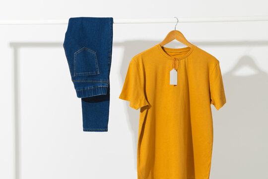 Yellow t shirt with tag and denim trousers on clothes rail with copy space on white background