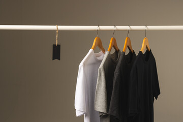 Four t shirts on hangers hanging from clothes rail and copy space on grey background