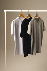 Fototapeta premium Three t shirts on hangers hanging from clothes rail and copy space on grey background