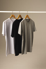 Three t shirts on hangers hanging from clothes rail and copy space on grey background