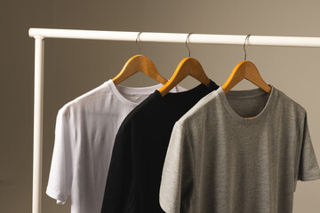 Fototapeta premium Three t shirts on hangers hanging from clothes rail and copy space on grey background