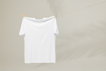 White t shirt hanging from clothes line with pegs and copy space on grey background