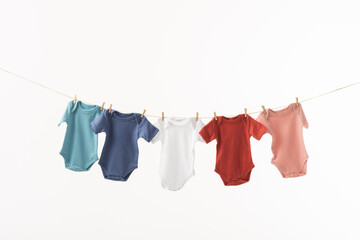 Multi coloured baby grows hanging from clothes line with pegs and copy space on white background
