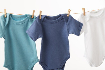 Three baby grows hanging from clothes line with pegs and copy space on white background