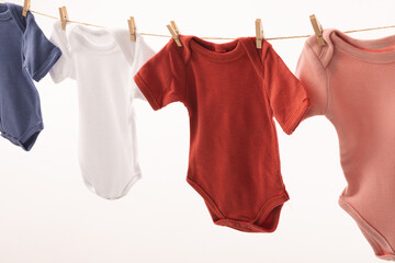 Multi coloured baby grows hanging from clothes line with pegs and copy space on white background