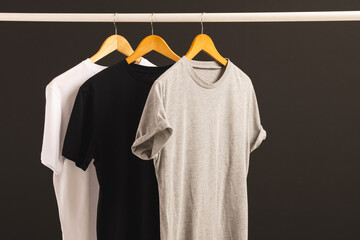 Fototapeta premium Three t shirts on hangers hanging from clothes rail and copy space on black background