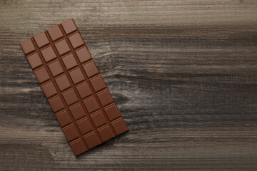 Delicious milk chocolate bar on wooden table, top view. Space for text