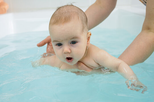 Baby swims in bathtub making primitive swimming strokes. Teacher makes session relaxed and fun for newborn based on natural baby reflexes