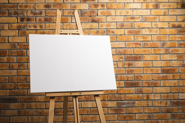 White canvas on wooden easel and copy space on brick wall background
