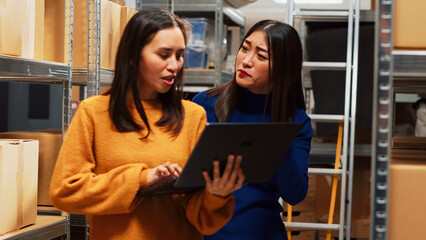 Female employees looking at logistics on laptop, working with quality control and supply chain management. Two women planning shipment, small business development in storage room.