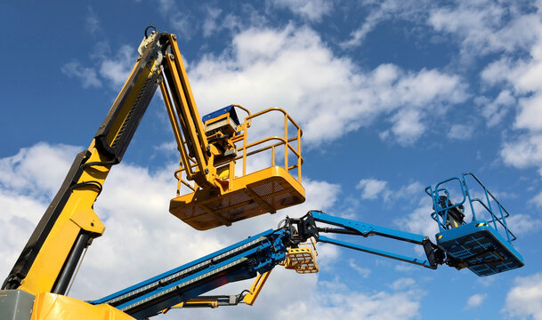 Aerial working platforms of cherry pickers against blue cloudy sky.