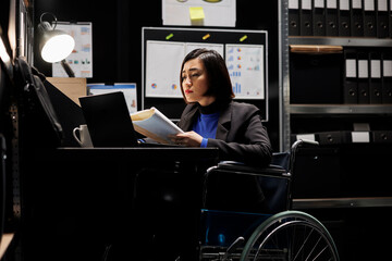 Asian accountant in wheelchair checking annual profit revenue documents before business consulting...