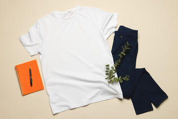 Flat lay of white t shirt, notebook and denim trousers with copy space on cream background