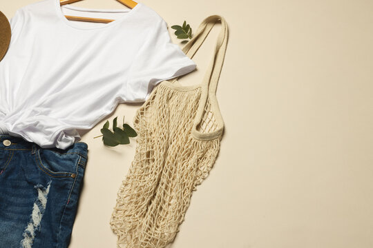 Flat lay of white t shirt, sunhat, net bag and denim skirt with copy space on cream background