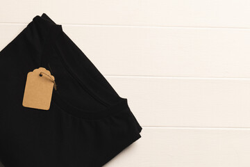 Close up of flat lay of black t shirt with tag and copy space on white boards background