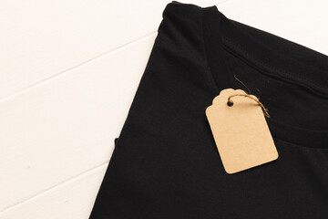 Close up of flat lay of black t shirt with tag and copy space on white boards background