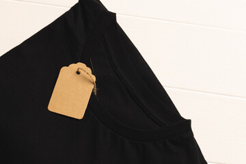 Close up of flat lay of black t shirt and tag with copy space on white board background