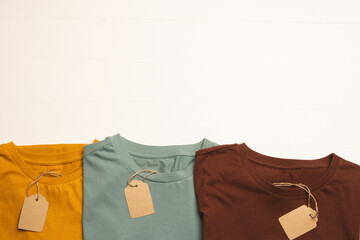 Close up of flat lay of three t shirts with tags and copy space on white boards background