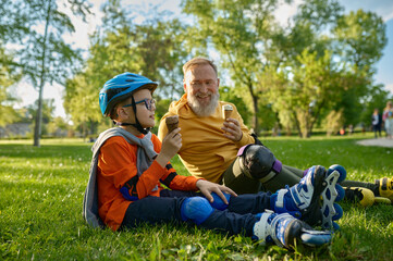 Happy grandpa and grandchild eating ice-cream after roller skating
