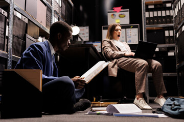 Overworked bookkeeper analyzing bureaucracy files in storage room, working late at night at...