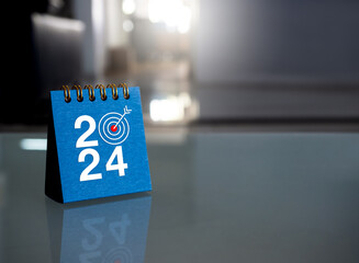 Happy new year 2024 banner background. 2024 numbers year with target icon on blue small desk calendar cover standing on glass table in office with copy space. Business goals and success concepts.