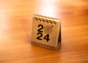 Happy new year 2024 banner background. 2024 numbers year with target icon on beige small desk calendar cover standing on wood table, minimal style. Business goals plan and success concepts.