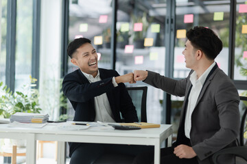 Excited happy young Asian two businessman winner and celebrating success at desk in office.
