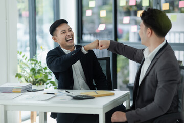 Excited happy young Asian two businessman winner and celebrating success at desk in office.