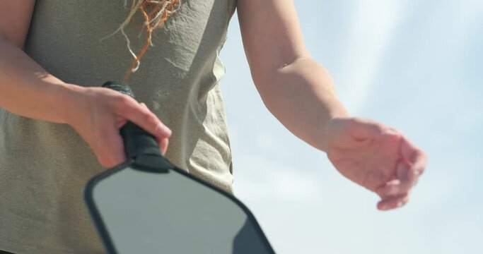 Pickleball paddle and yellow ball close up, woman playing pickleball game, hitting pickleball yellow ball with paddle, outdoor sport leisure activity.