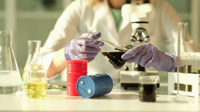 Scientist in chemical industrial laboratory holds black liquid crude oil in flask. Main stages of quality control of petroleum products