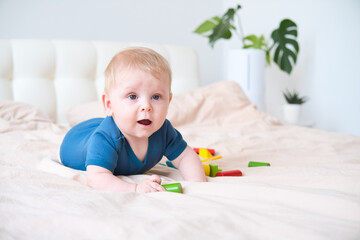 Naklejka premium baby boy in blue bodysuit playing with colorful wooden eco toys on bed