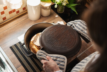 Fresh baked homemade bread pulled from cast iron into the bowl. Woman holding hot kitchen utensils,...