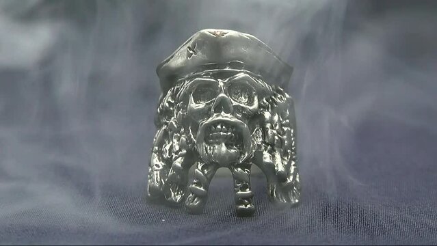 A pirate skull ring is shrouded in gray smoke on a black background in a video	

