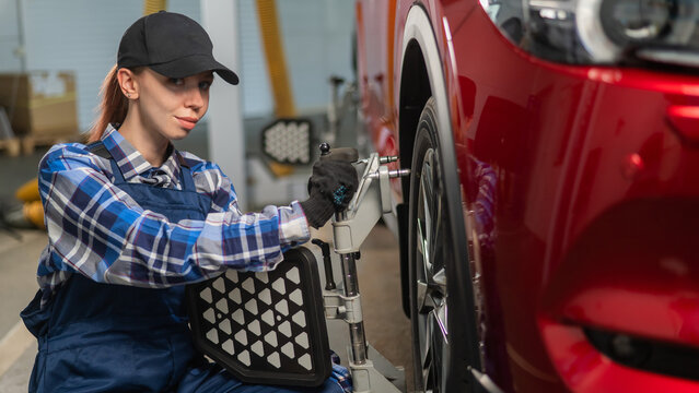 A female auto mechanic makes a camber. Woman working in a car service.