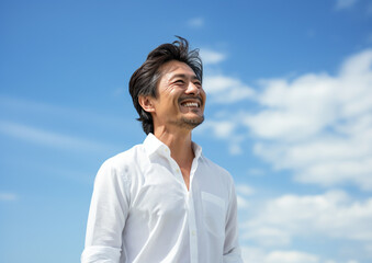 空を背景に微笑むアジア人のシニア男性