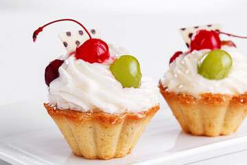 Beautiful cream cakes with cherries and grapes on a plate on a white background