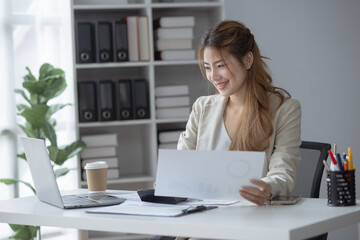 Asian businesswoman holding papers preparing report at office desk, business finance and accounting concept.